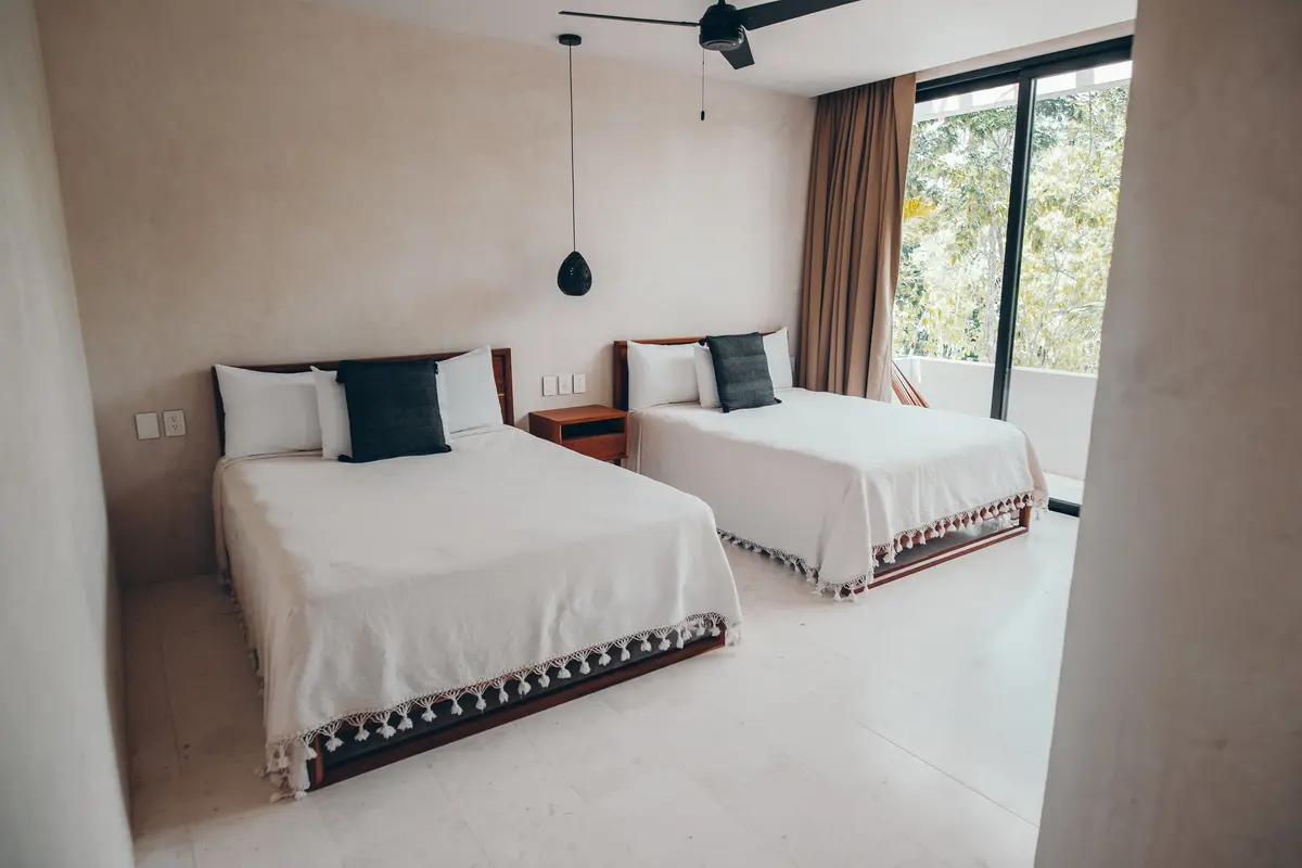 Casa Thomas guest bedroom with two beds, dark gray pillows and a sliding door open to a terrace